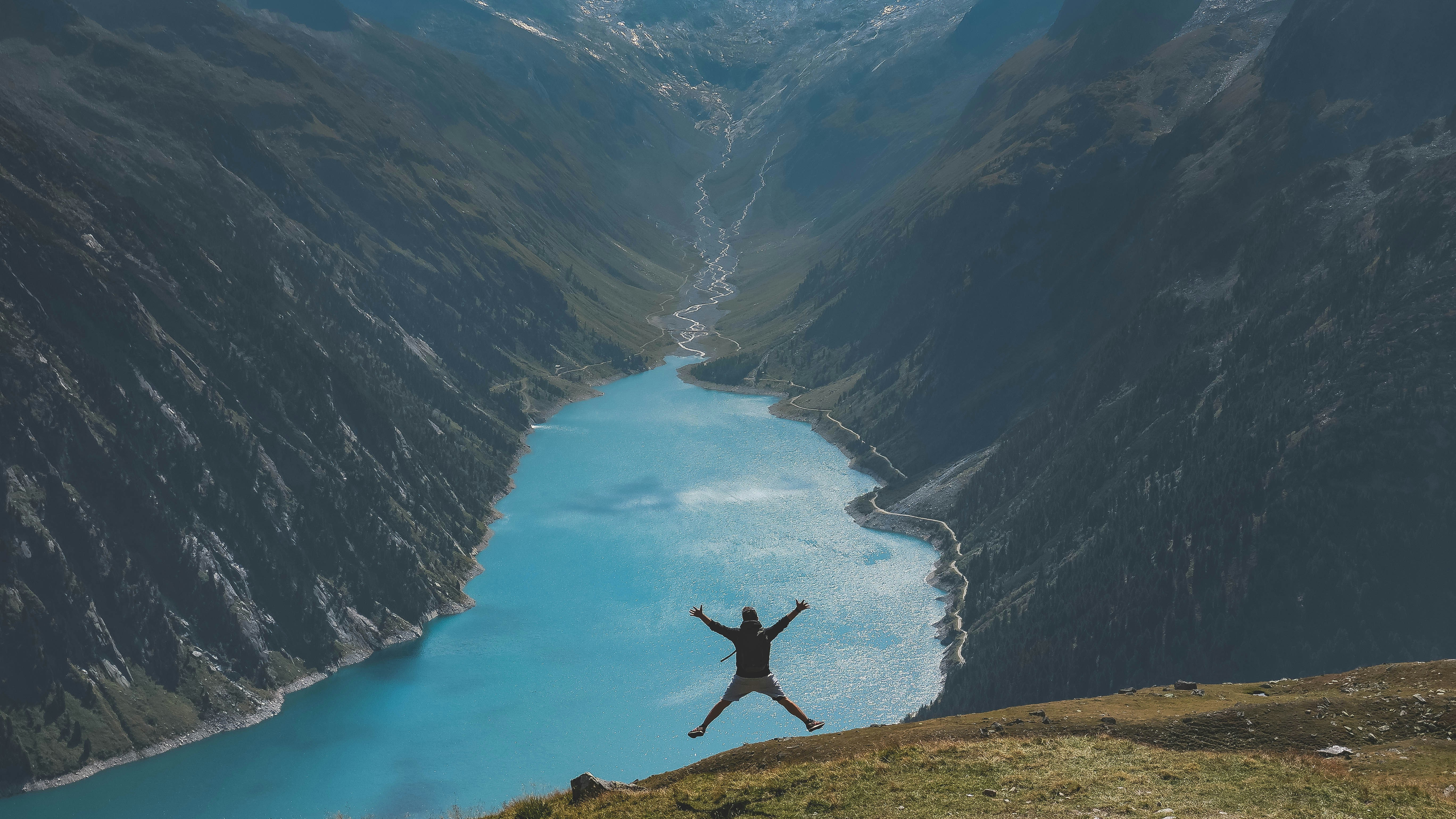 Privilégier les moments, plus que les produits Un homme fait un saut de joie devant un lac au coeur des montages, la photo est prise de loin pour montrer le paysage